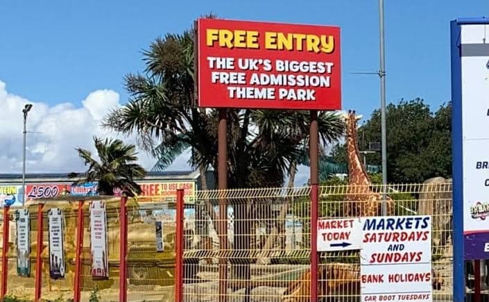 The roadside sign: Free Entry, the UK's biggest free admission theme park, in yellow and white on red.