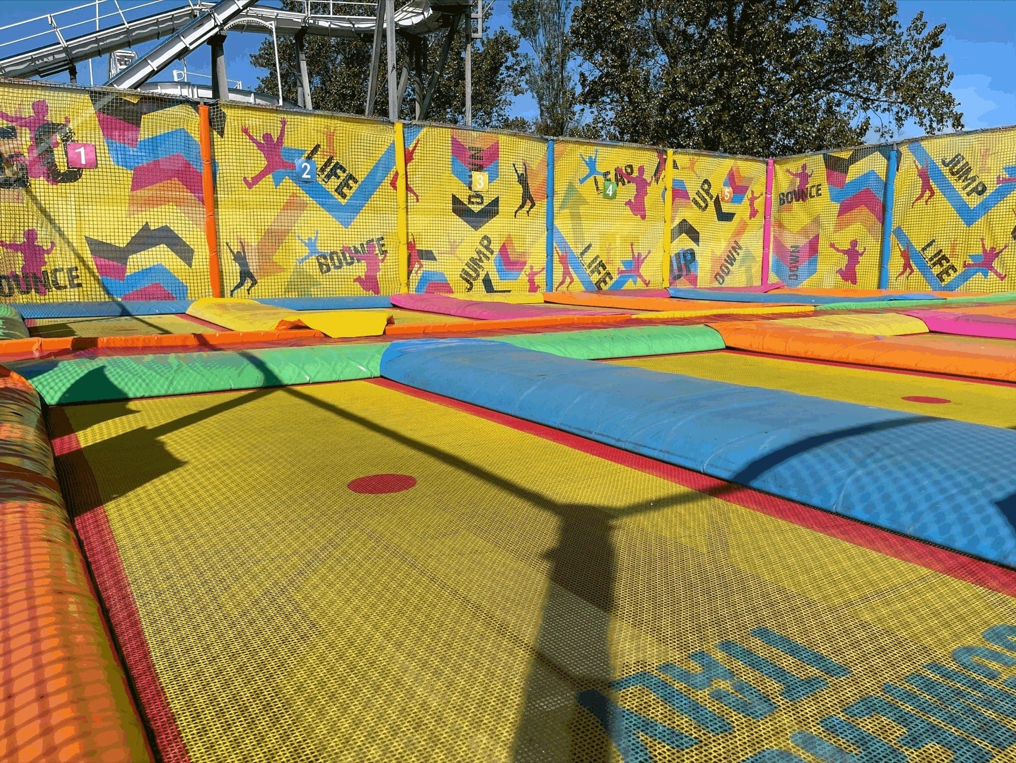 The trampoline area, with yellow netting printed with jumping silhouettes, chevrons and the words Bounce, Jump and Life, and numbered bays.