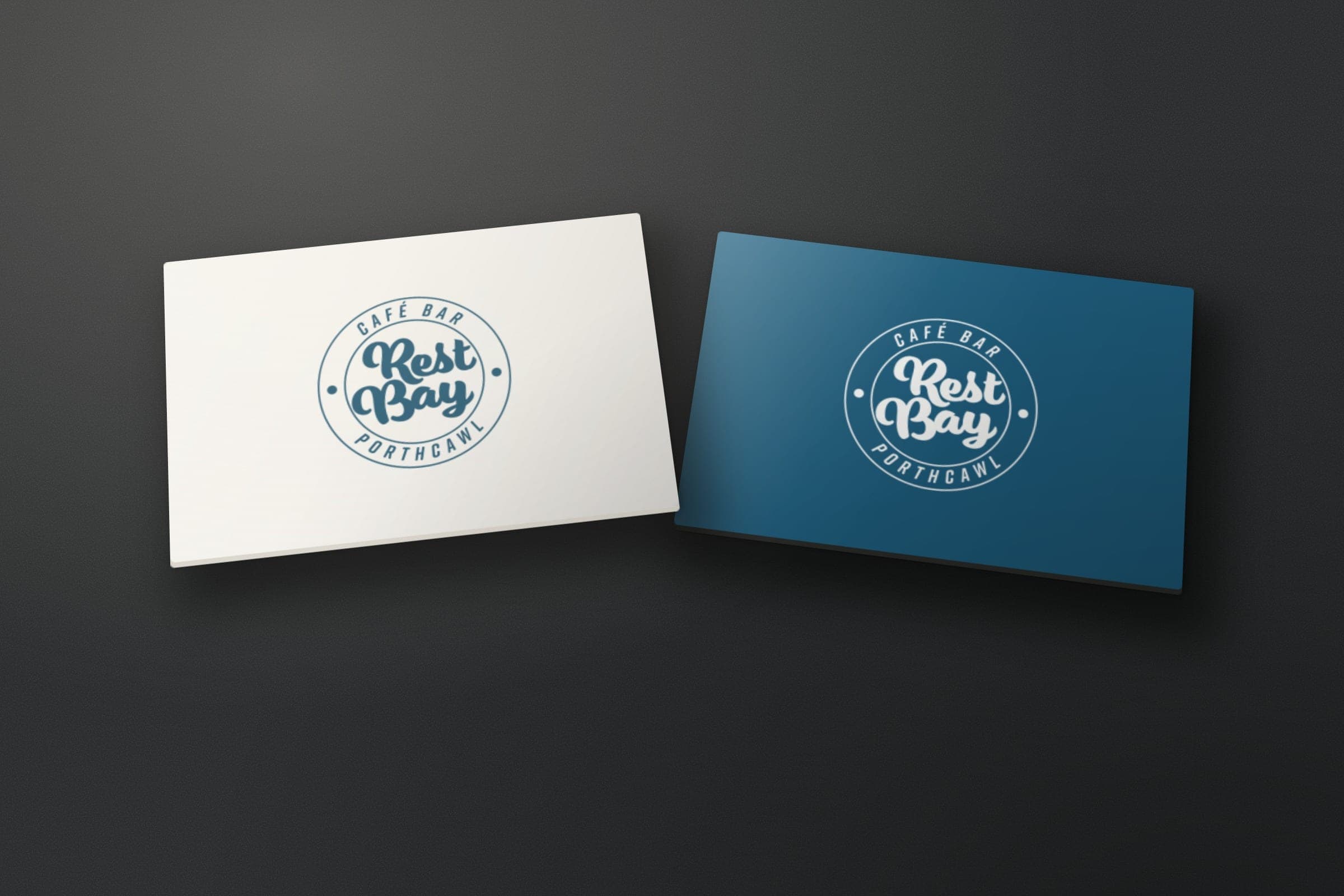 Mockup: the Rest Bay Café Bar roundel on two cards, in blue on white and in white on blue.